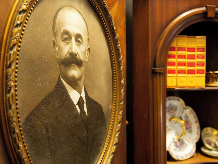 A framed portrait with a vintage appearance, a wooden shelf with ceramic dishes, and a box of red and yellow items.