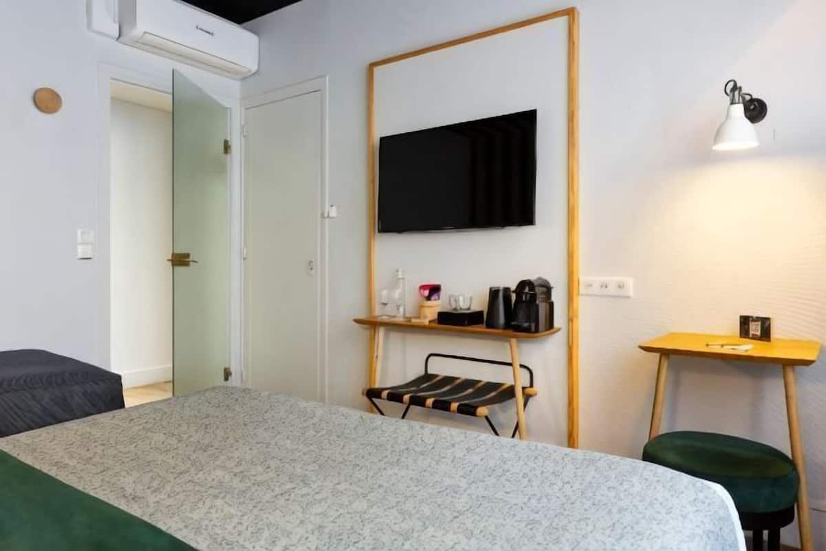 Une chambre d’hôtel avec un lit, un téléviseur fixé au mur, une petite table avec une lampe et une chaise.