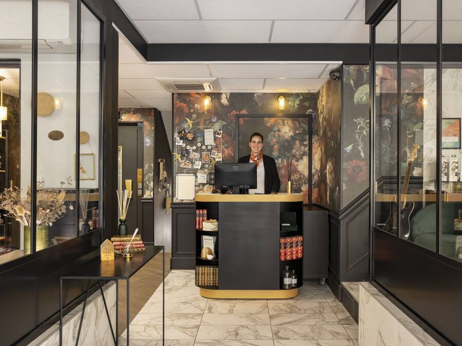 Un mostrador de recepción con una computadora, una vitrina de vidrio con varios objetos y una pared decorativa con motivos florales.