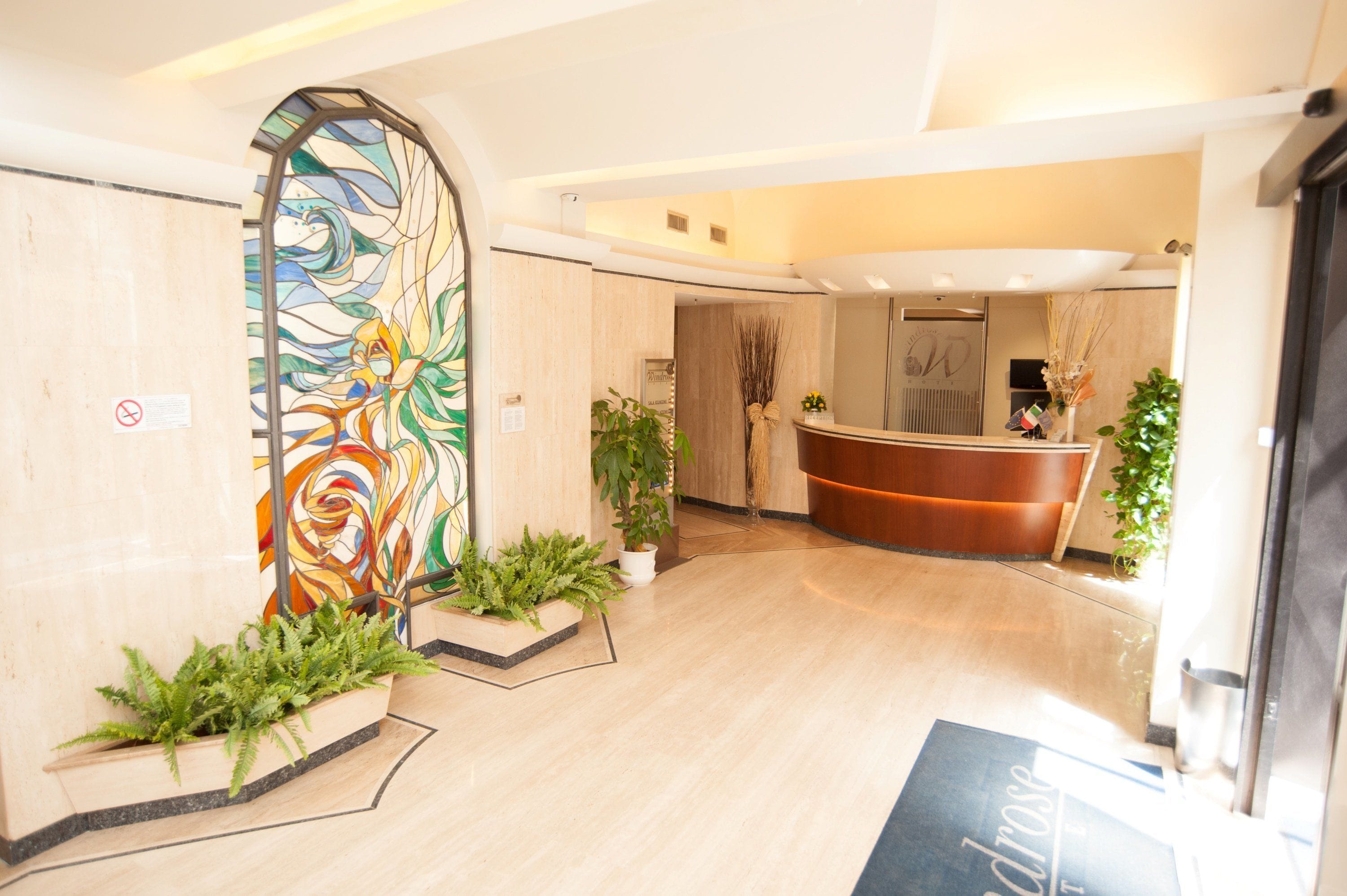 Un hall d’hôtel comprenant un comptoir d’accueil, une grande fresque murale abstraite et des plantes en pot.