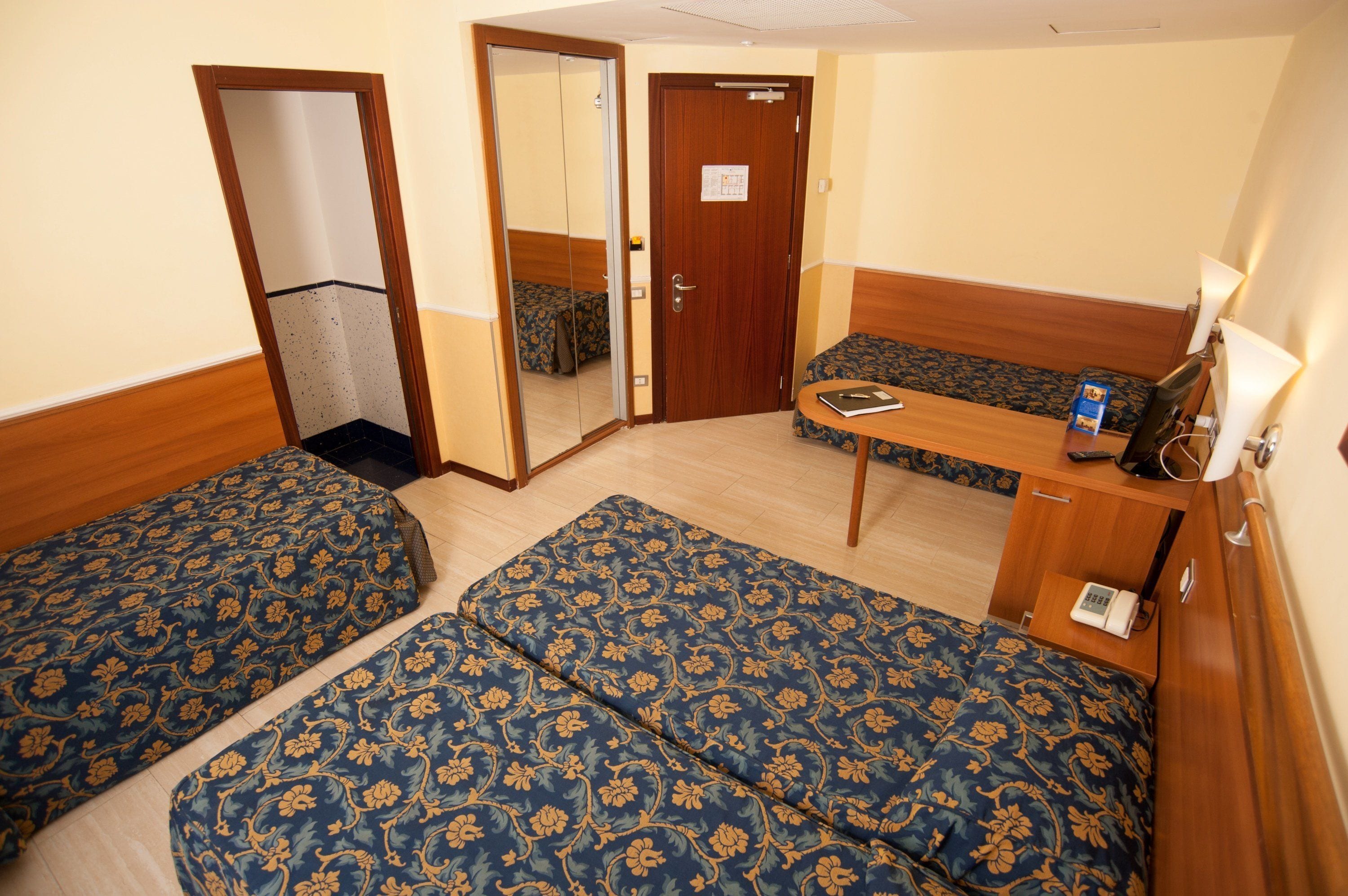 A hotel room with two single beds, a wooden desk, a mirror, and a door.