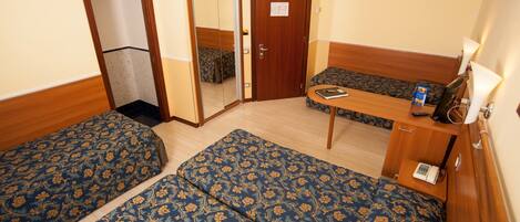 A hotel room with two single beds, a wooden desk, a mirror, and a door.