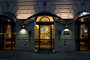 L’entrée d’un hôtel, ornée d’une grande baie vitrée aux motifs colorés, d’une enseigne portant le nom « Windrose », et dotée d’une architecture moderne avec des portes en arc de cercle.