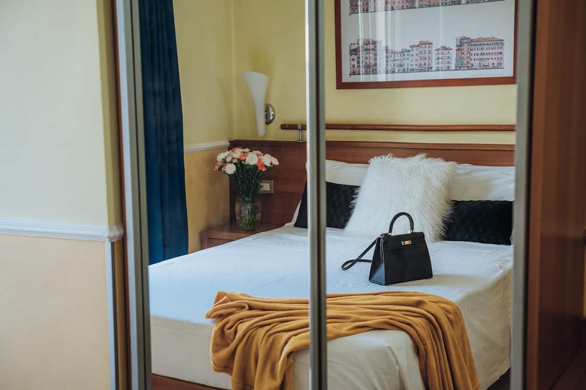 Une chambre d’hôtel avec un lit, une table de chevet, un vase de fleurs et un tableau encadré représentant un paysage urbain accroché au mur.
