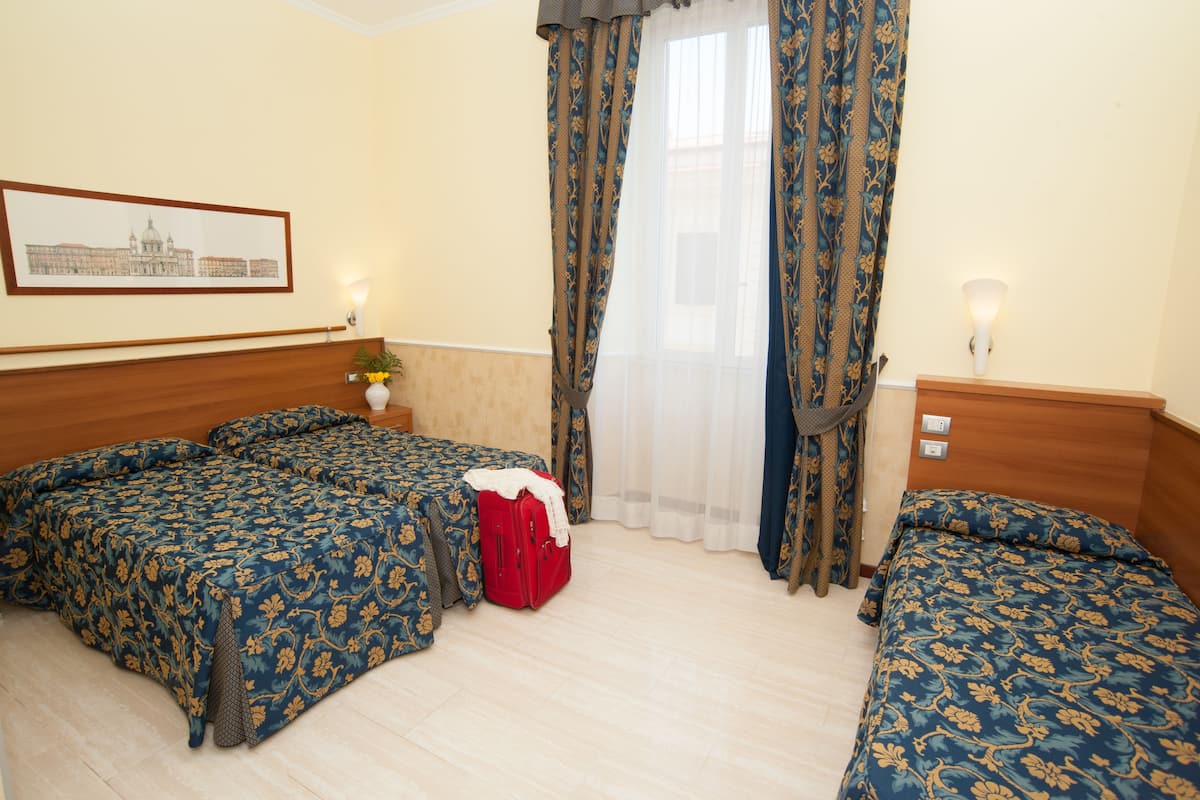 Une chambre d’hôtel avec deux lits, une valise rouge et un tableau encadré accroché au mur.