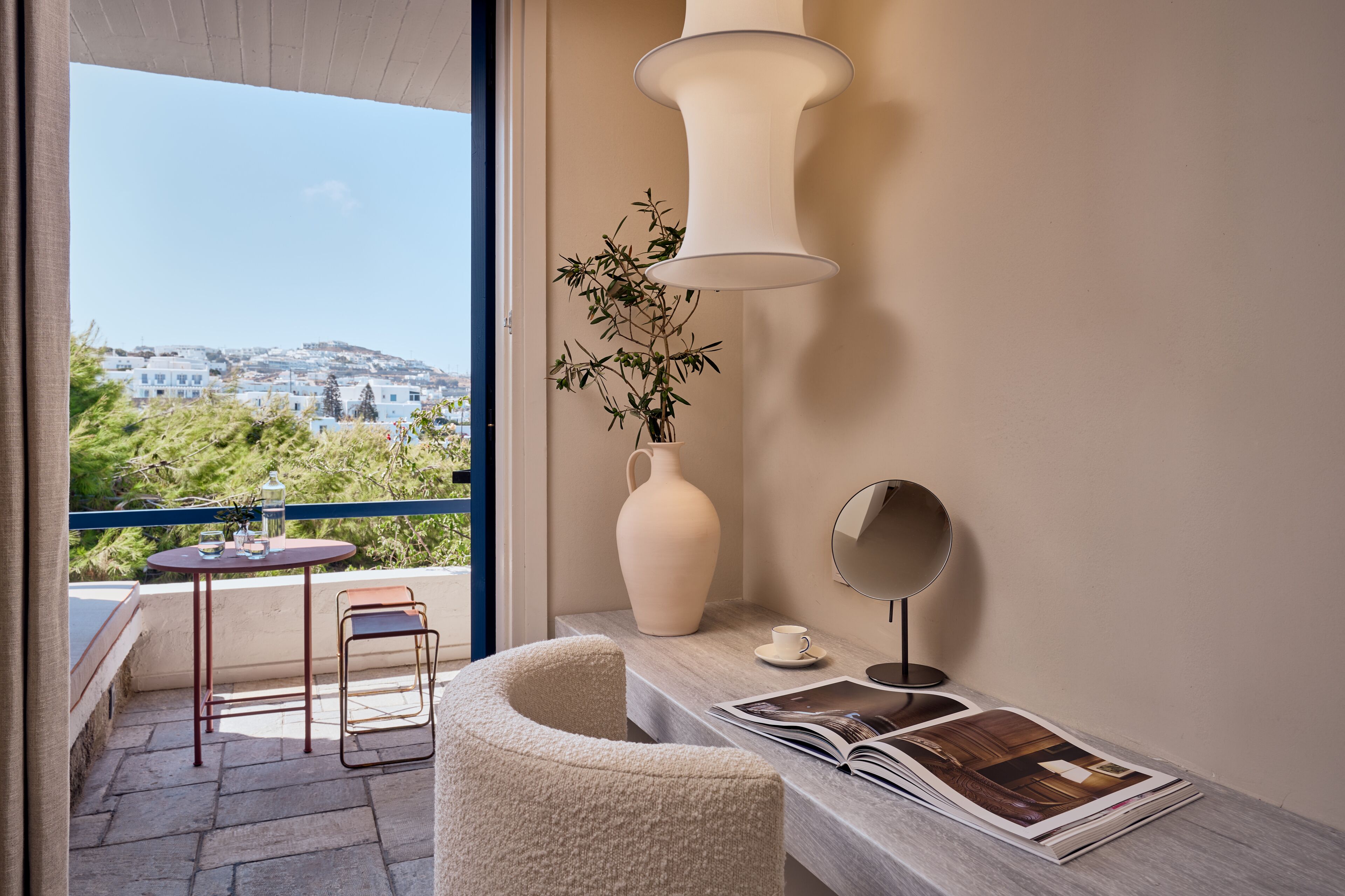 A balcony with a table, chairs, a vase with plants, a lamp, and a magazine.