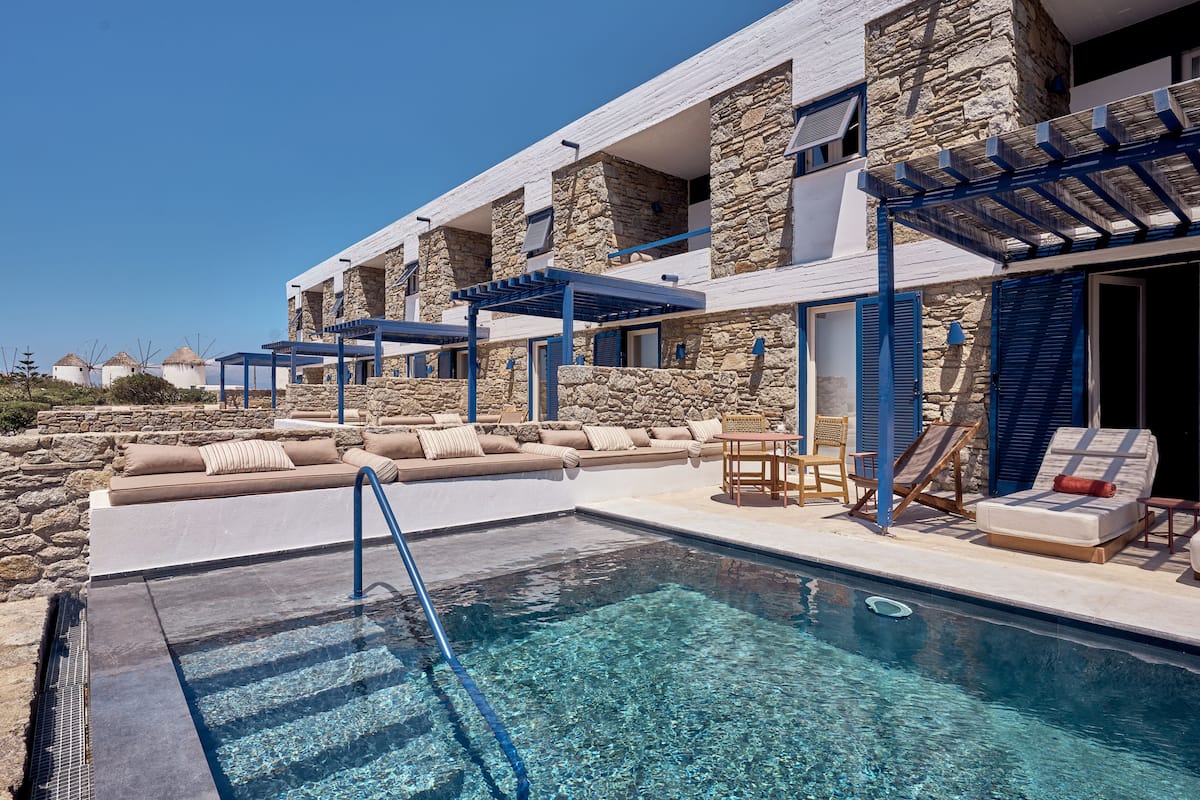 A pool area with a clear blue pool, lounge chairs, and a stone building with balconies.