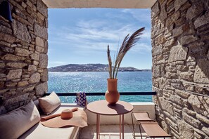 A stone-walled balcony with a round table, a vase with dried plants, and a view of the sea and distant hills. - Mykonos Theoxenia, a Member of Design Hotels (Mykonos)