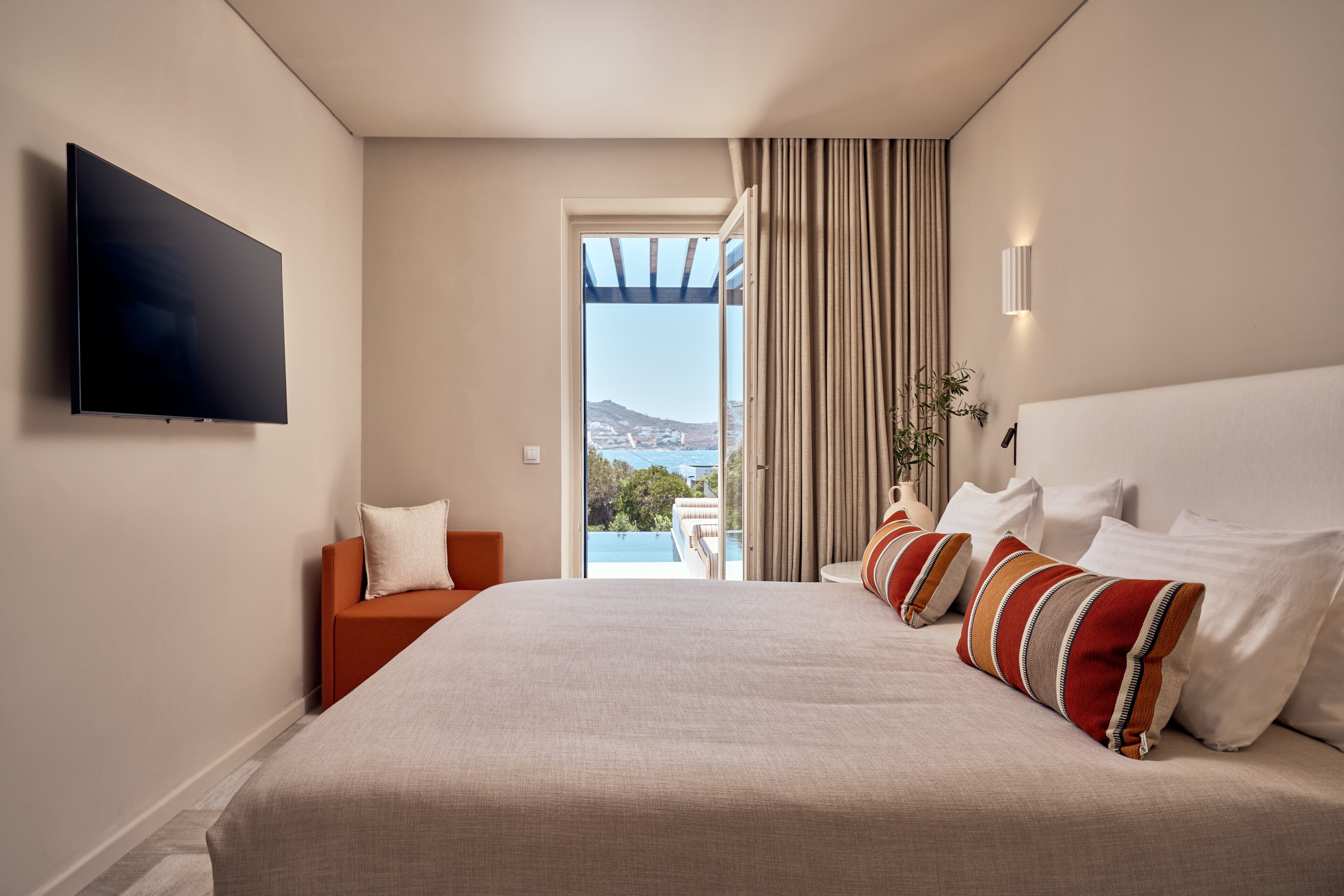 Een hotelkamer met een groot bed, een aan de muur bevestigde televisie, uitzicht op de omgeving en een klein zithoekje.