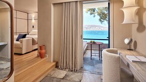 A modern hotel room with a balcony, a sofa, a table, and a view of the sea.