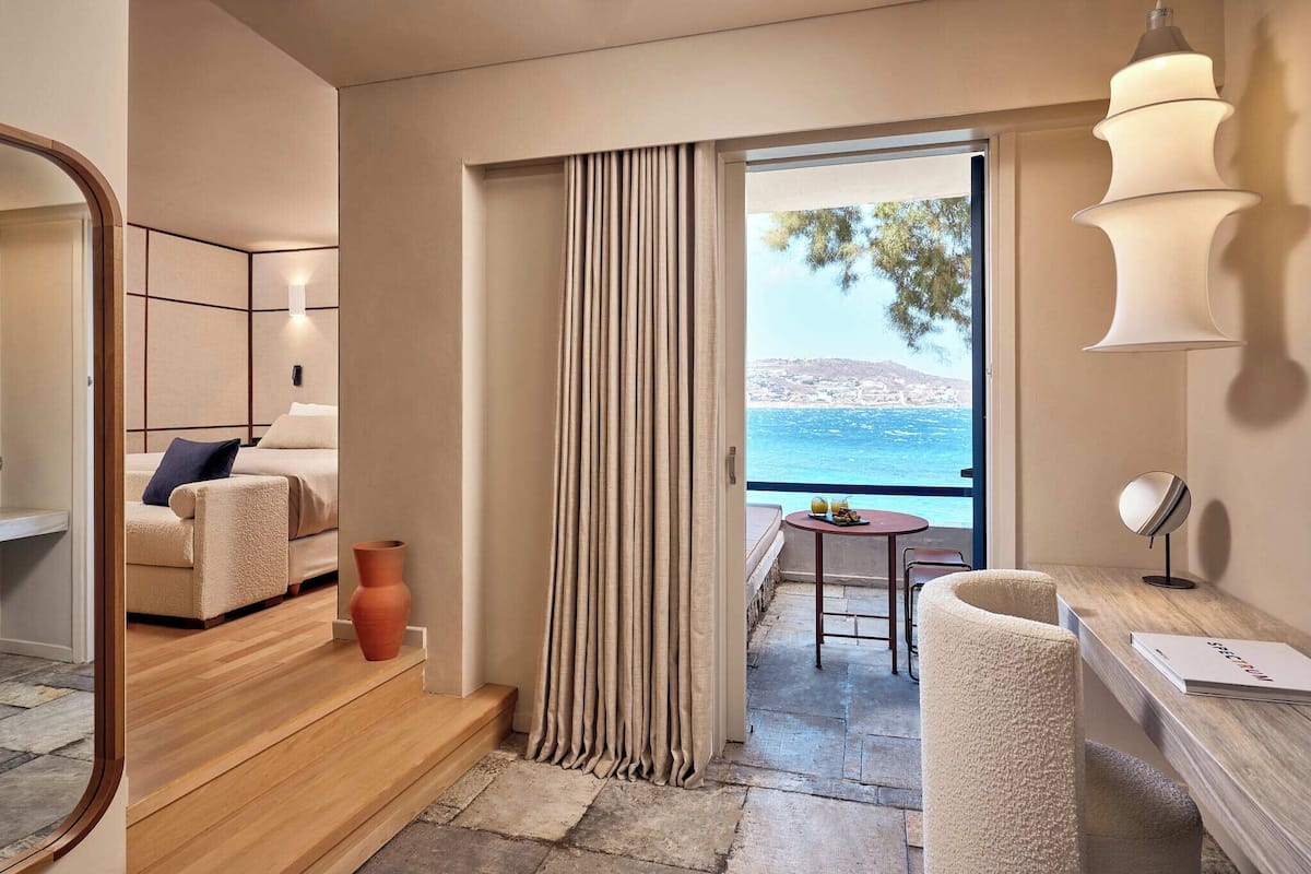 A modern hotel room with a balcony, a sofa, a table, and a view of the sea.