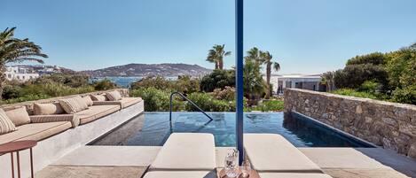 A poolside area with lounge chairs and a table, overlooking a scenic coastal view.