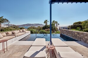 A poolside area with lounge chairs and a table, overlooking a scenic coastal view. - Mykonos Theoxenia, a Member of Design Hotels (Mykonos)