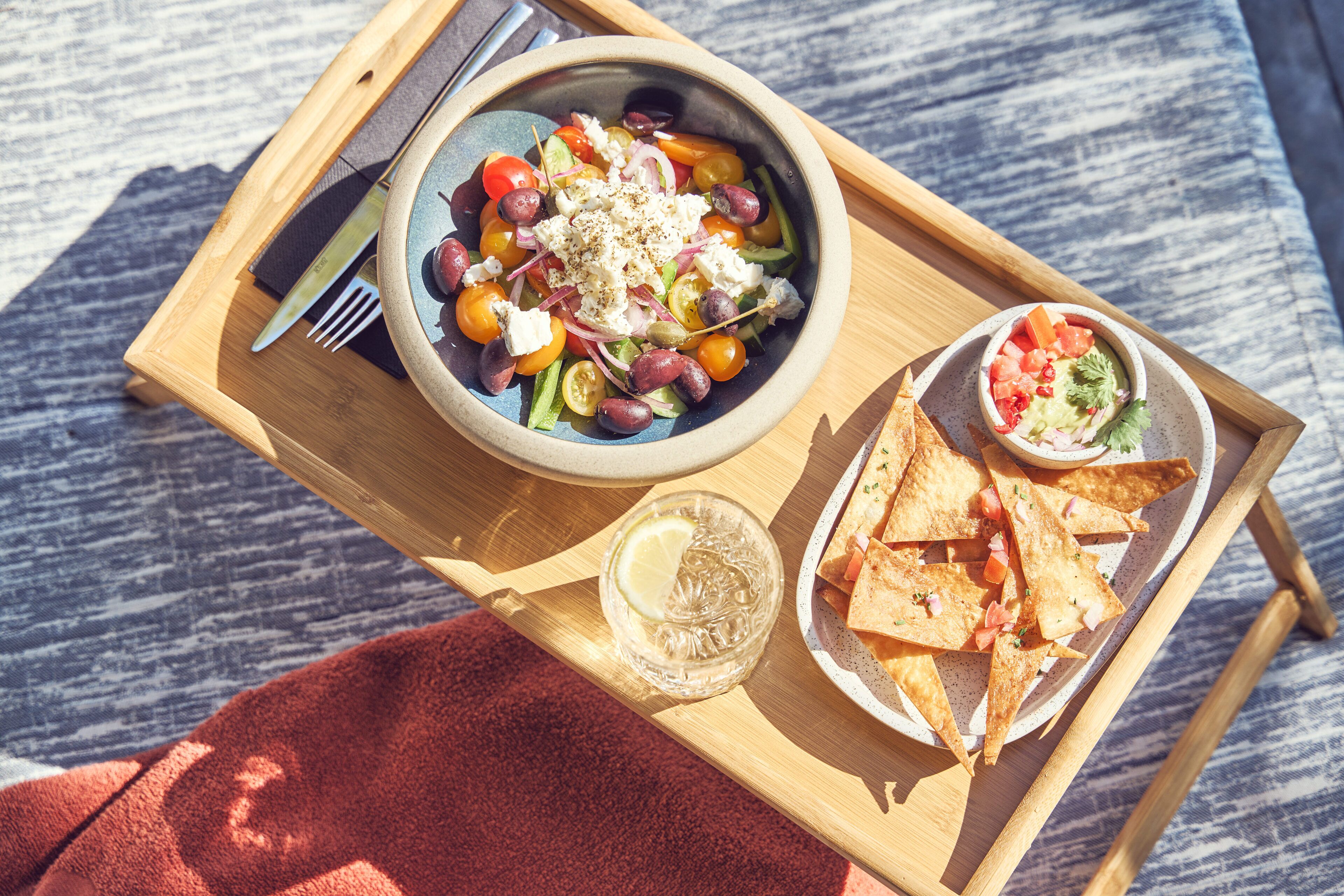A wooden tray with a bowl of salad, tortilla chips, and a small bowl of salsa.