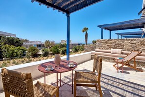 A terrace with a round table, wicker chairs, a cushioned sofa, and a stone wall. - Mykonos Theoxenia, a Member of Design Hotels (Mykonos)