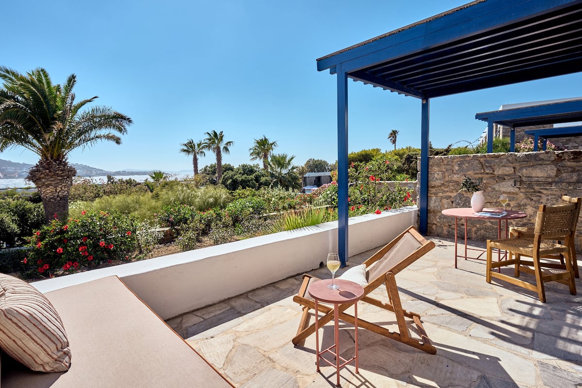 A terrace with a view of the sea, stone flooring, wooden lounge chairs, and a pergola.