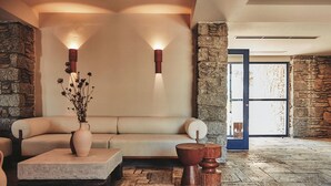 A cozy room with a stone wall, a cushioned bench, a vase with dried flowers, and a wooden stool.