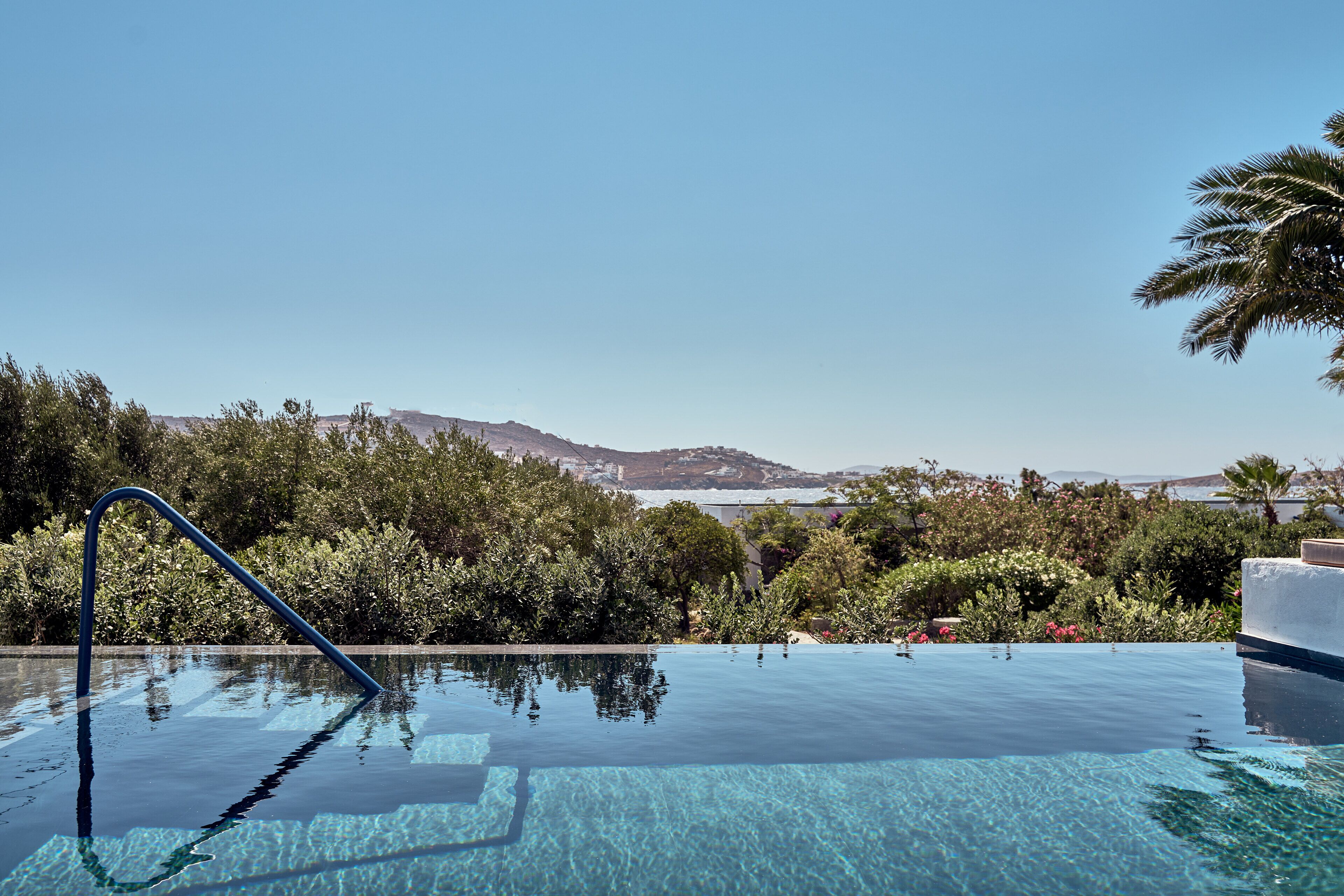 Una piscina infinita con vistas despejadas al océano y colinas al fondo.