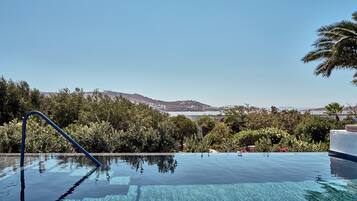 Una piscina infinita con vistas despejadas al océano y colinas al fondo.