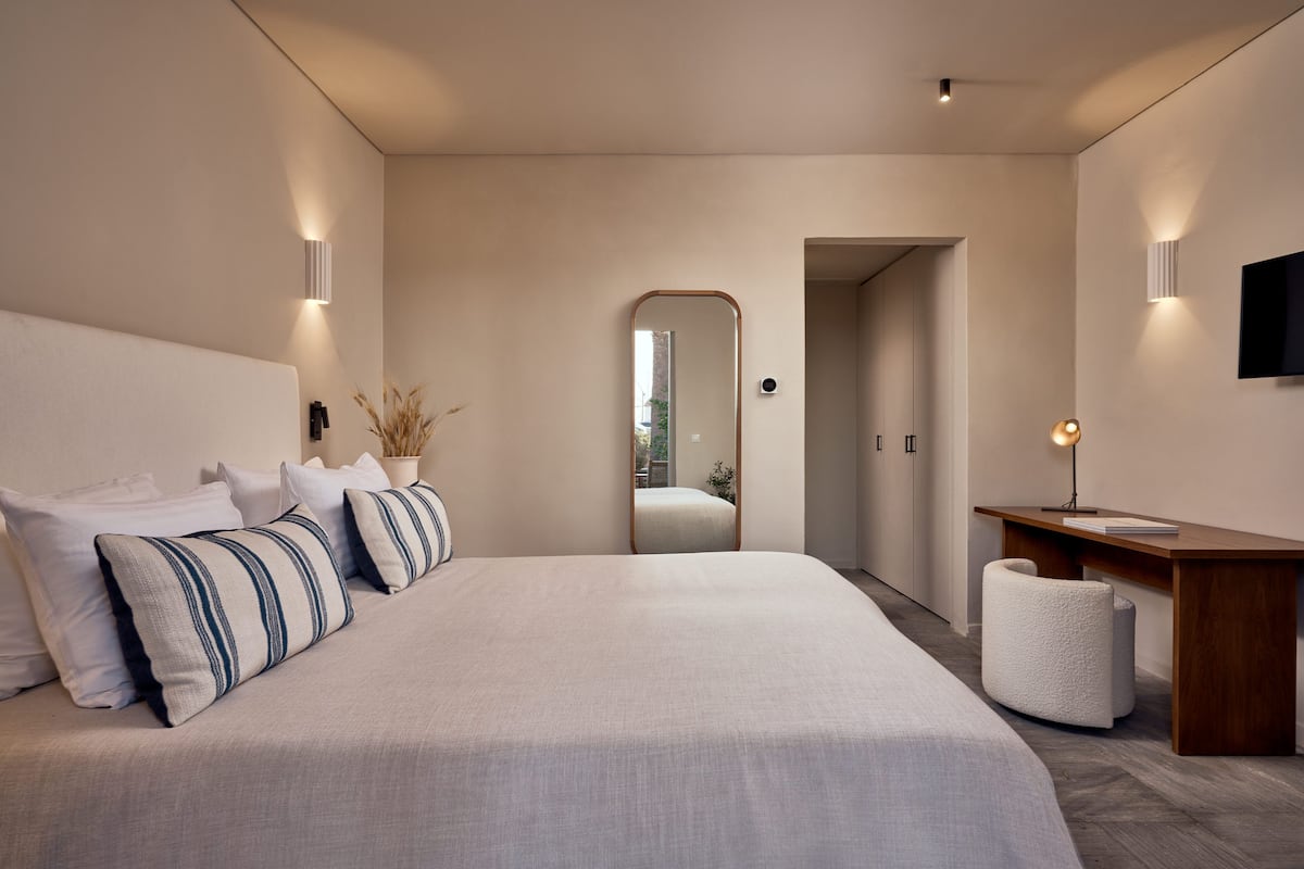 A modern bedroom with a large bed, bedside tables, a desk, and a mirror.