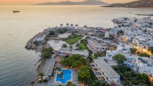 A coastal hotel with a swimming pool, multiple buildings, and a view of the sea.