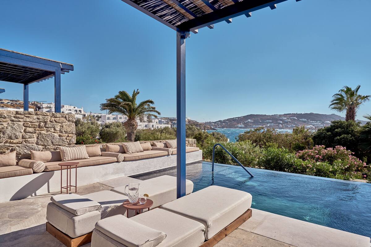 An infinity pool with a view of the sea, a sun lounger, and a seating area with cushions.