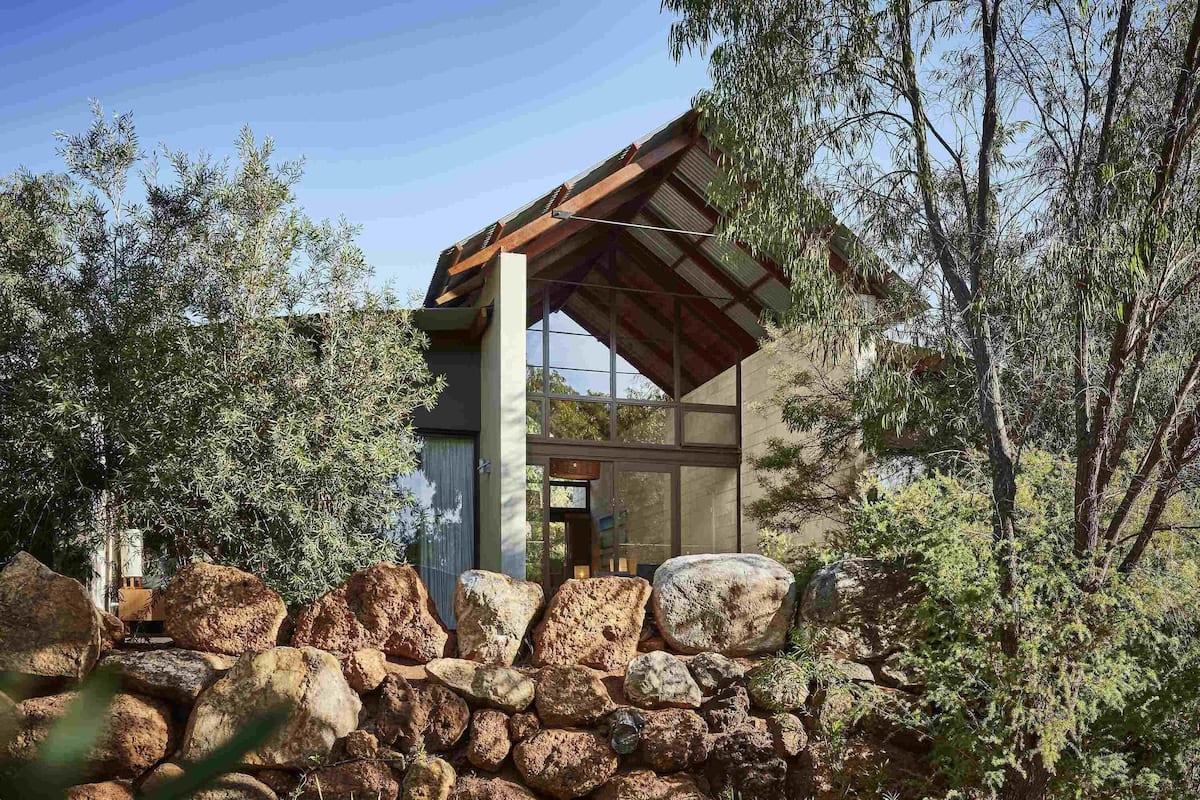 Un edificio moderno con un muro de piedra y rocas grandes al frente, rodeado de árboles.