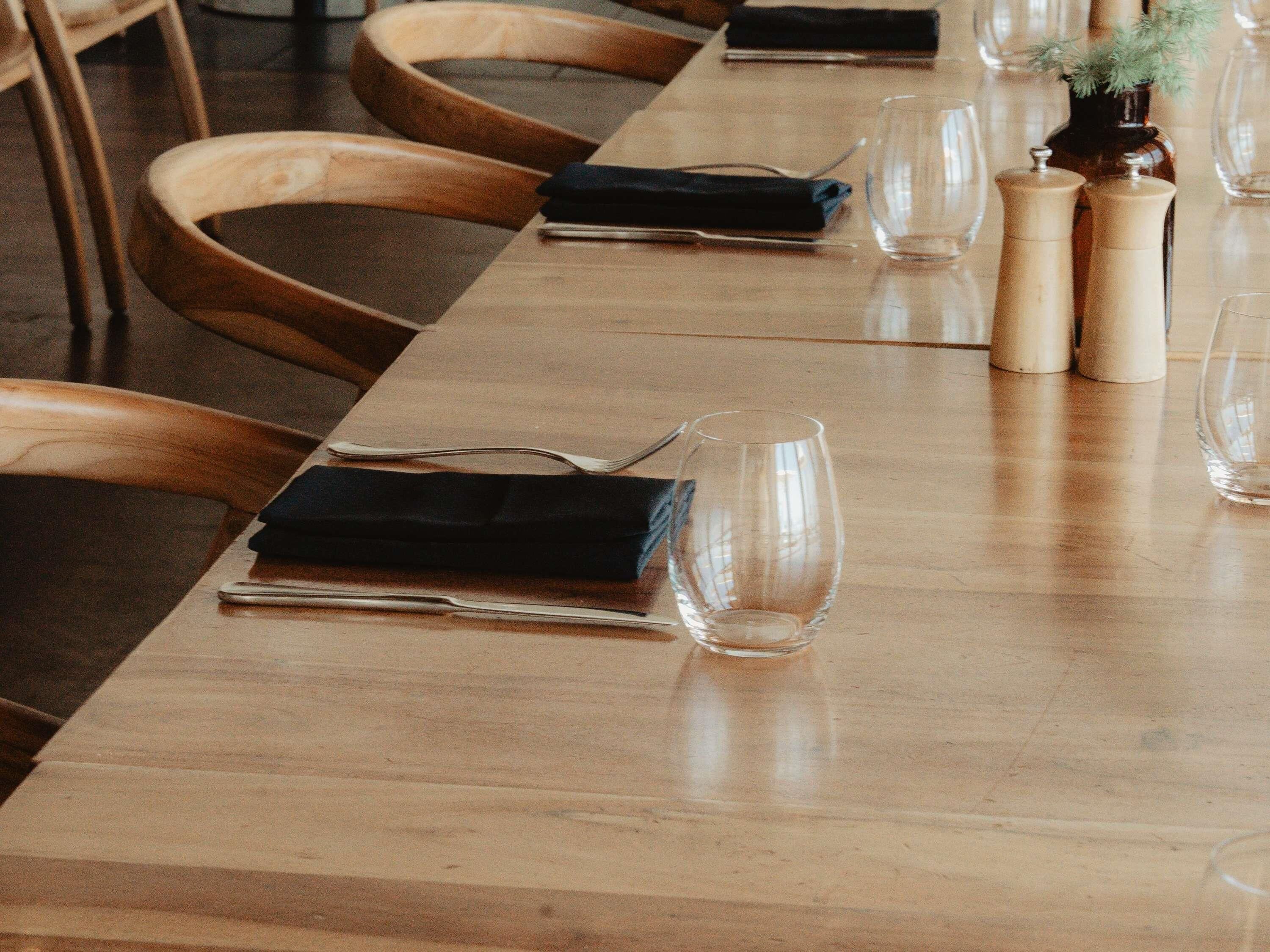 A long wooden table with chairs, clear glassware, and a small vase with greenery.