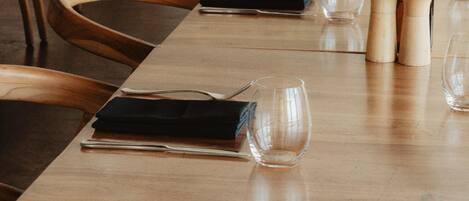 A long wooden table with chairs, clear glassware, and a small vase with greenery.