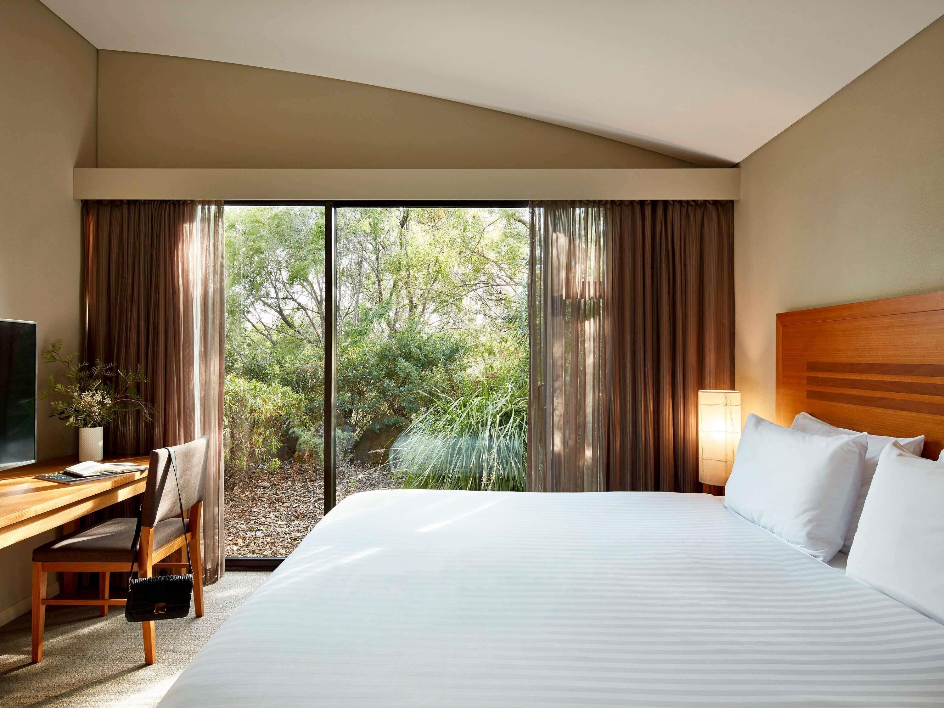A hotel room with a bed, a desk, a chair, a TV, and a window with curtains.
