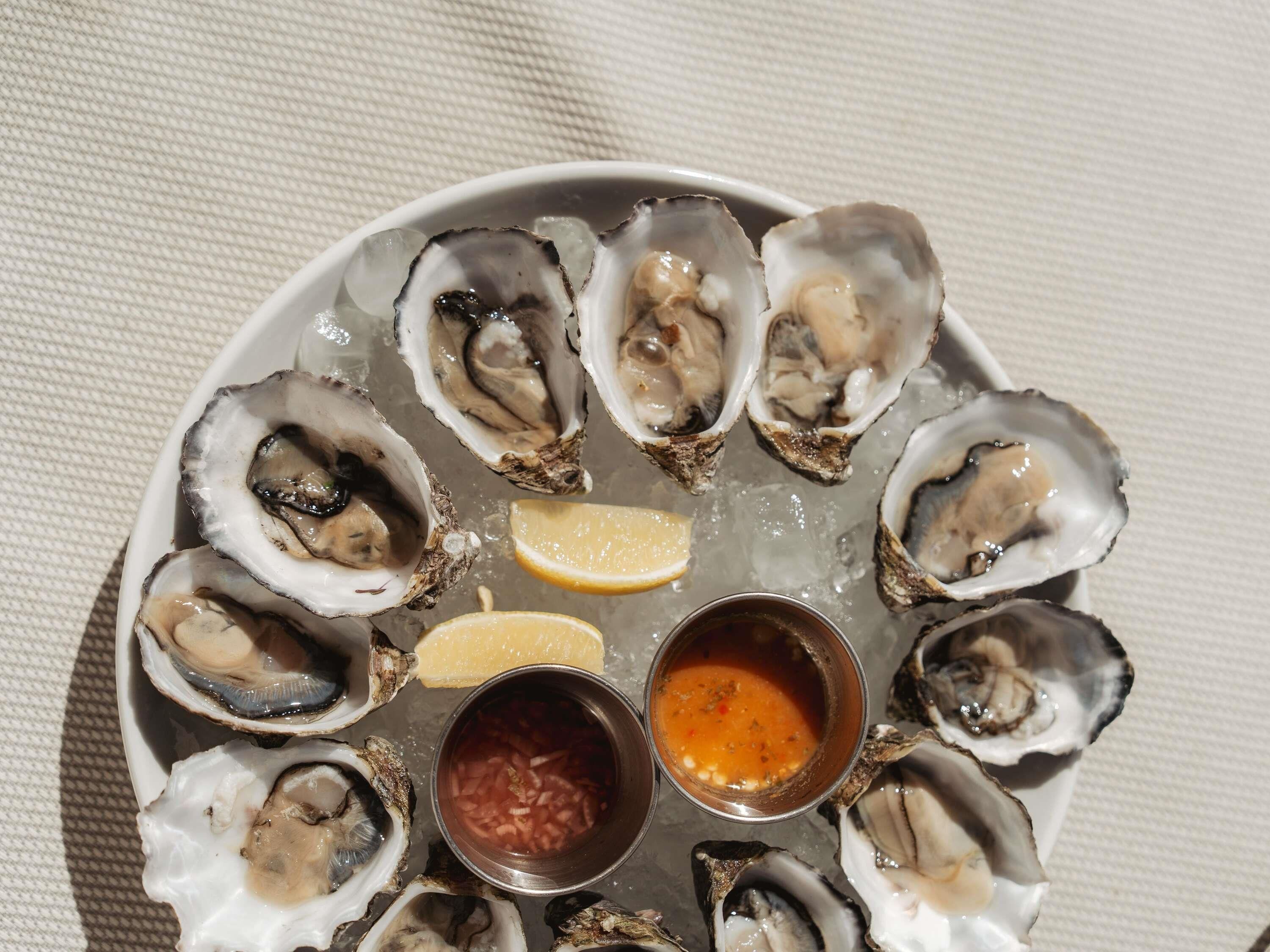 Une assiette d’huîtres, accompagnée de quartiers de citron et de deux sauces pour tremper.