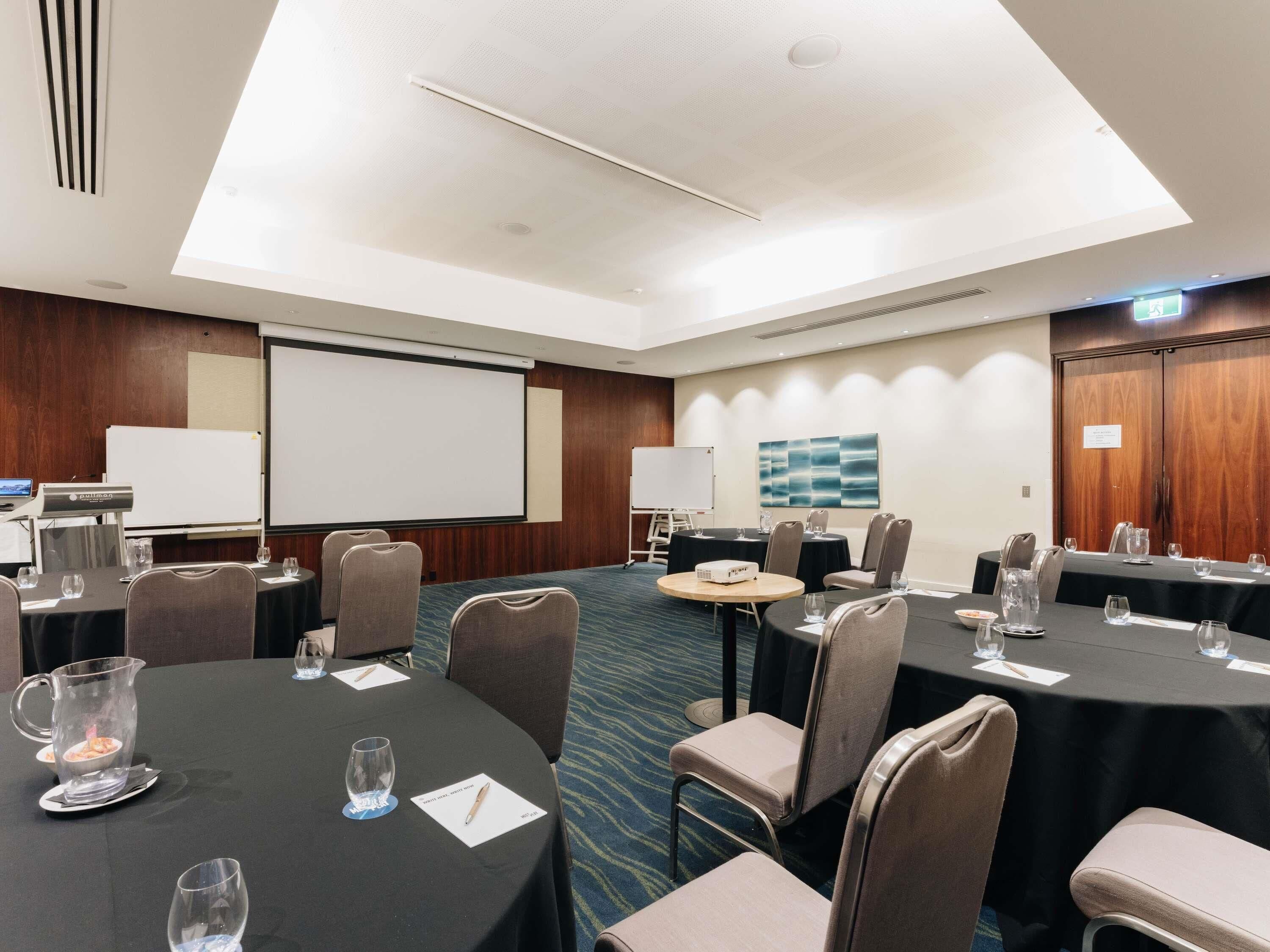 A conference room with tables, chairs, a projector screen, and a large window.