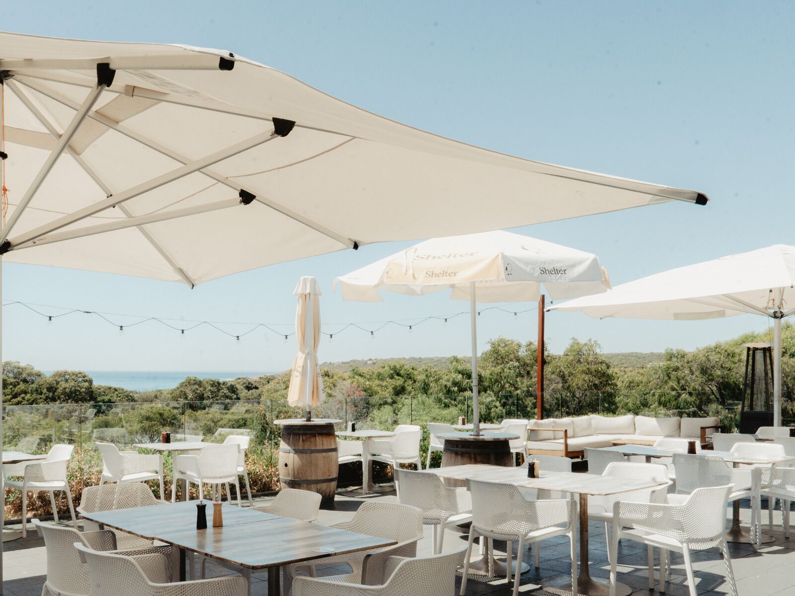 Un espacio al aire libre con mesas y sillas, sombrillas y vistas al mar.