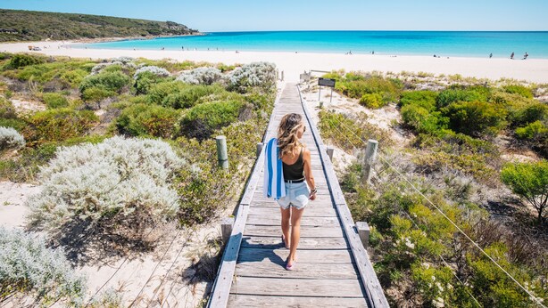 Un paseo marítimo de madera que conduce a una playa con aguas azules cristalinas y orillas de arena.