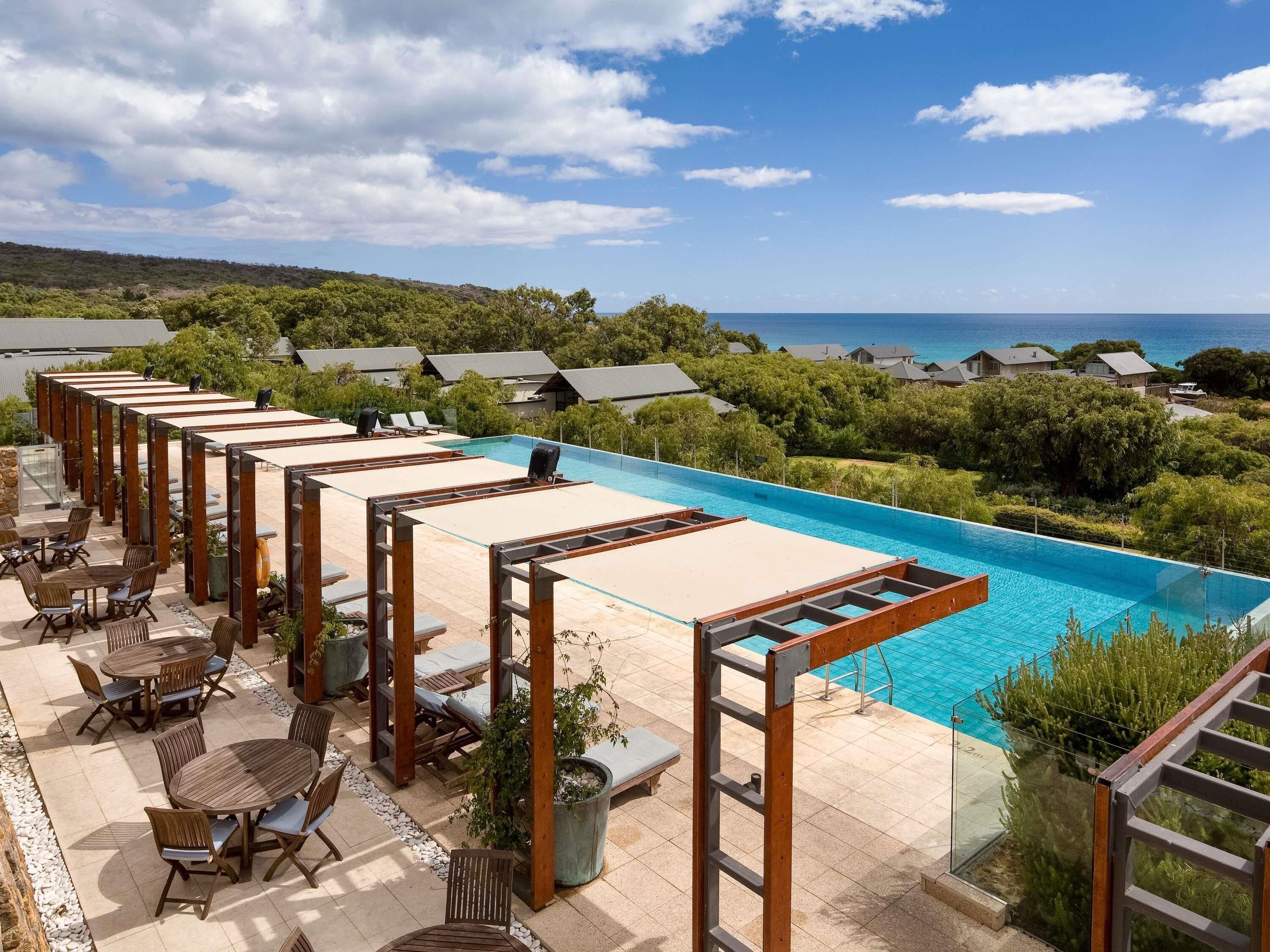 Ein Poolbereich mit Liegestühlen und Tischen, mit Blick auf ein klares, blaues Schwimmbecken und das Meer.