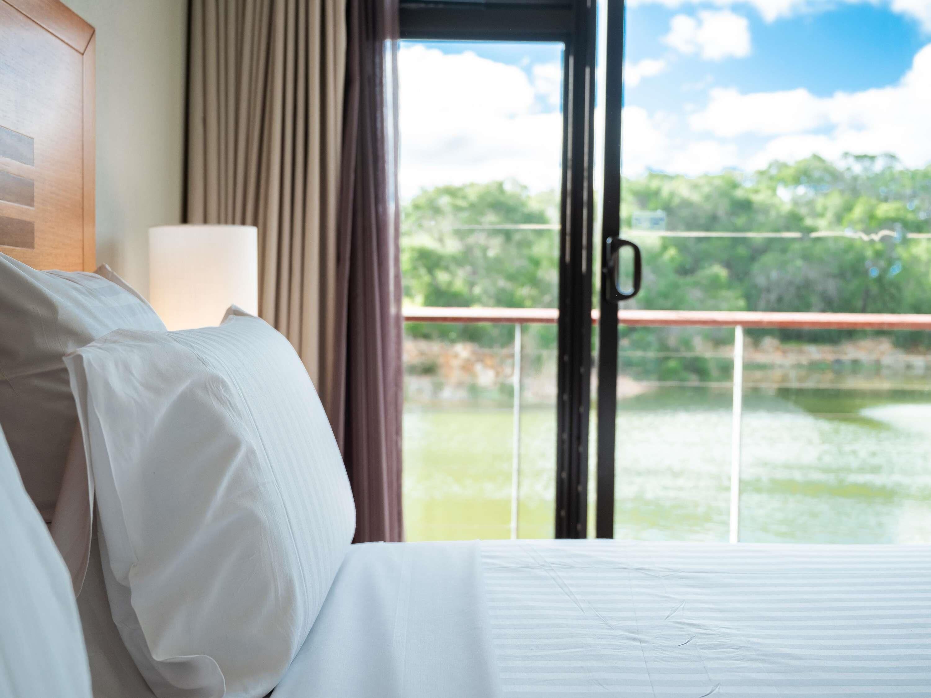 A hotel room with a bed, a nightstand, a lamp, and a view of a lake through a glass door.