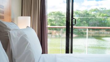 A hotel room with a bed, a nightstand, a lamp, and a view of a lake through a glass door.
