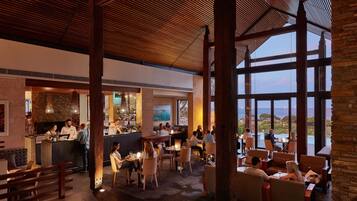 A spacious indoor area with a bar, seating arrangements, and large windows offering a view of the outdoors.