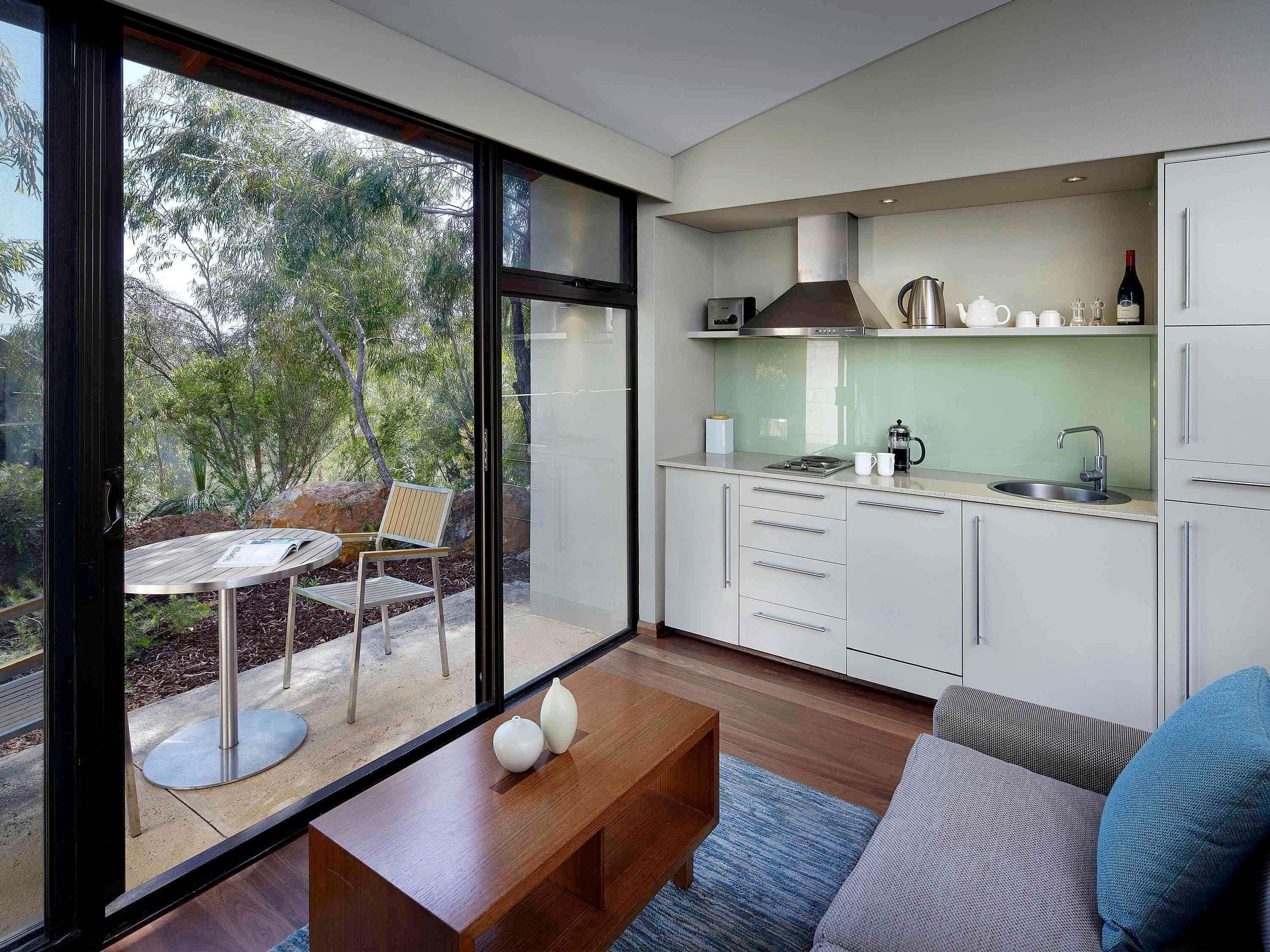A modern kitchen with white cabinets, a stainless steel range hood, and a large window overlooking a garden.