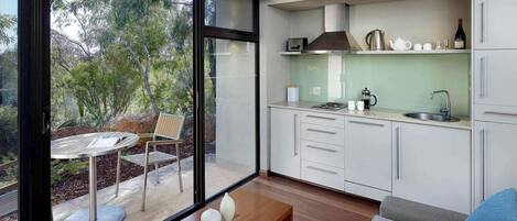 A modern kitchen with white cabinets, a stainless steel range hood, and a large window overlooking a garden.