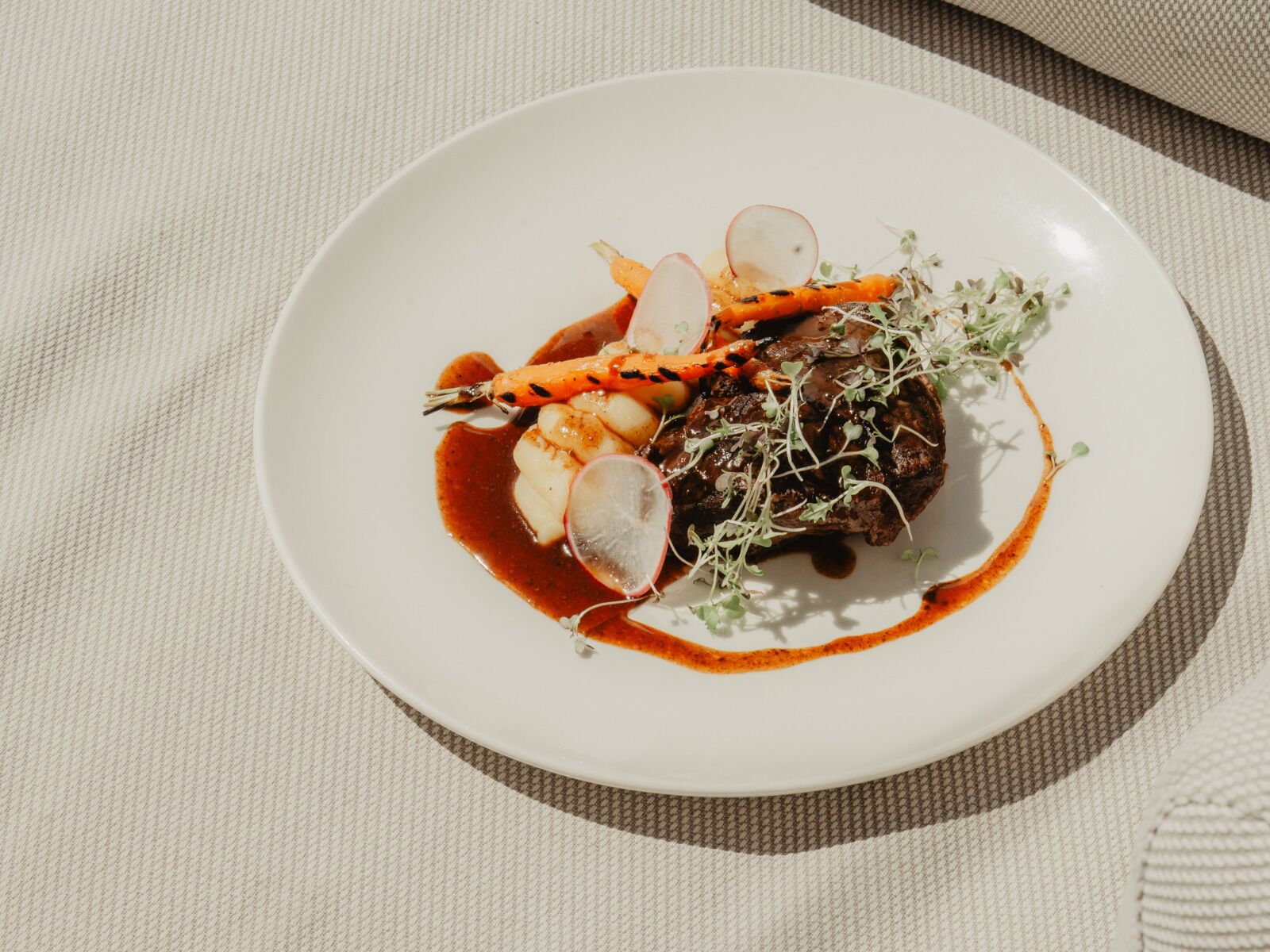 Un plato blanco con guiso de carne, verduras y salsa.