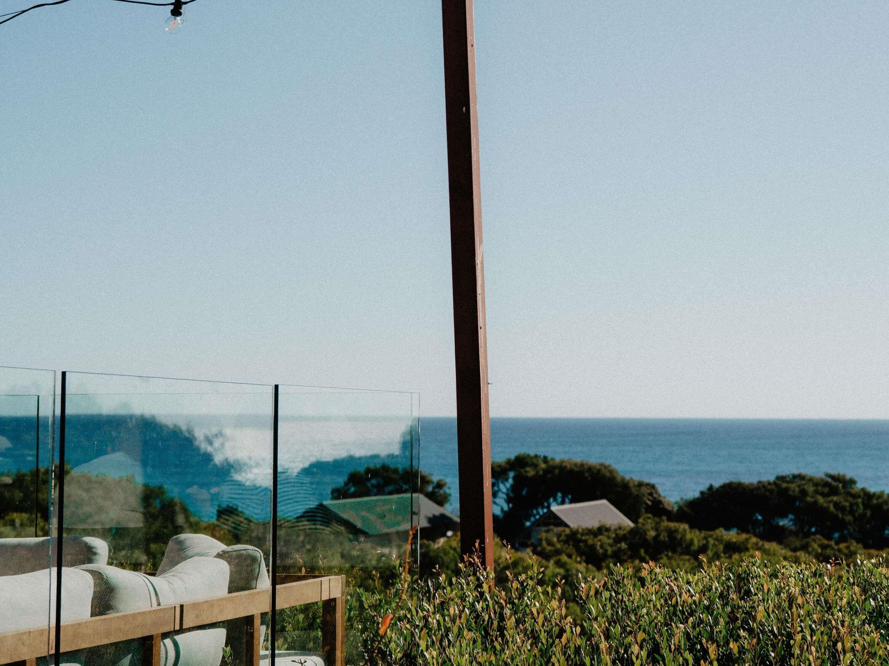 Un espacio moderno para sentarse al aire libre con vistas despejadas al océano y colinas lejanas.