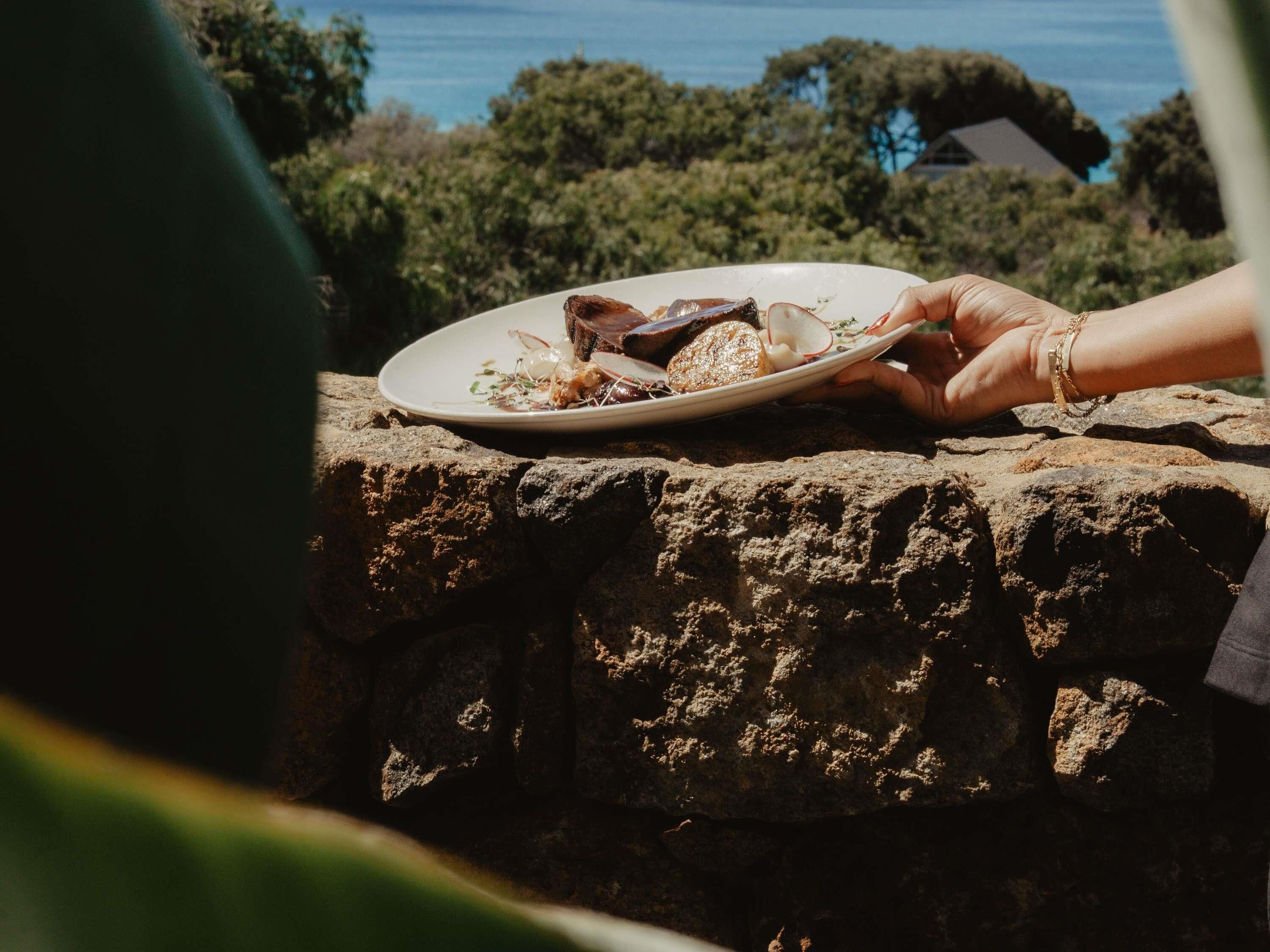 A person holding a plate with food on a stone ledge.