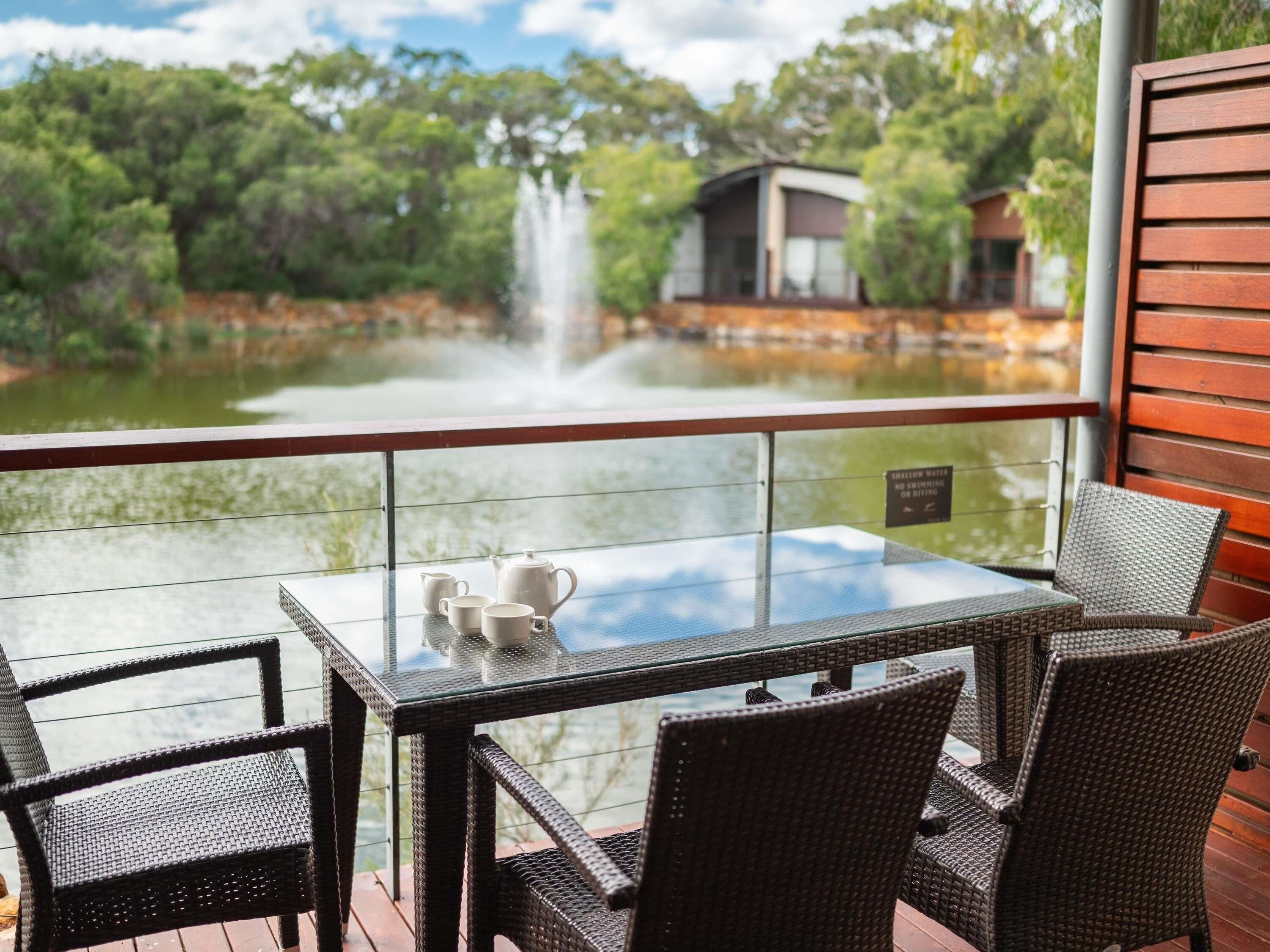 Ein Glastisch mit Stühlen auf einer Terrasse mit Blick auf einen Teich und einen Wasserfall, mit einem Schild, das für flaches Wasser warnt.