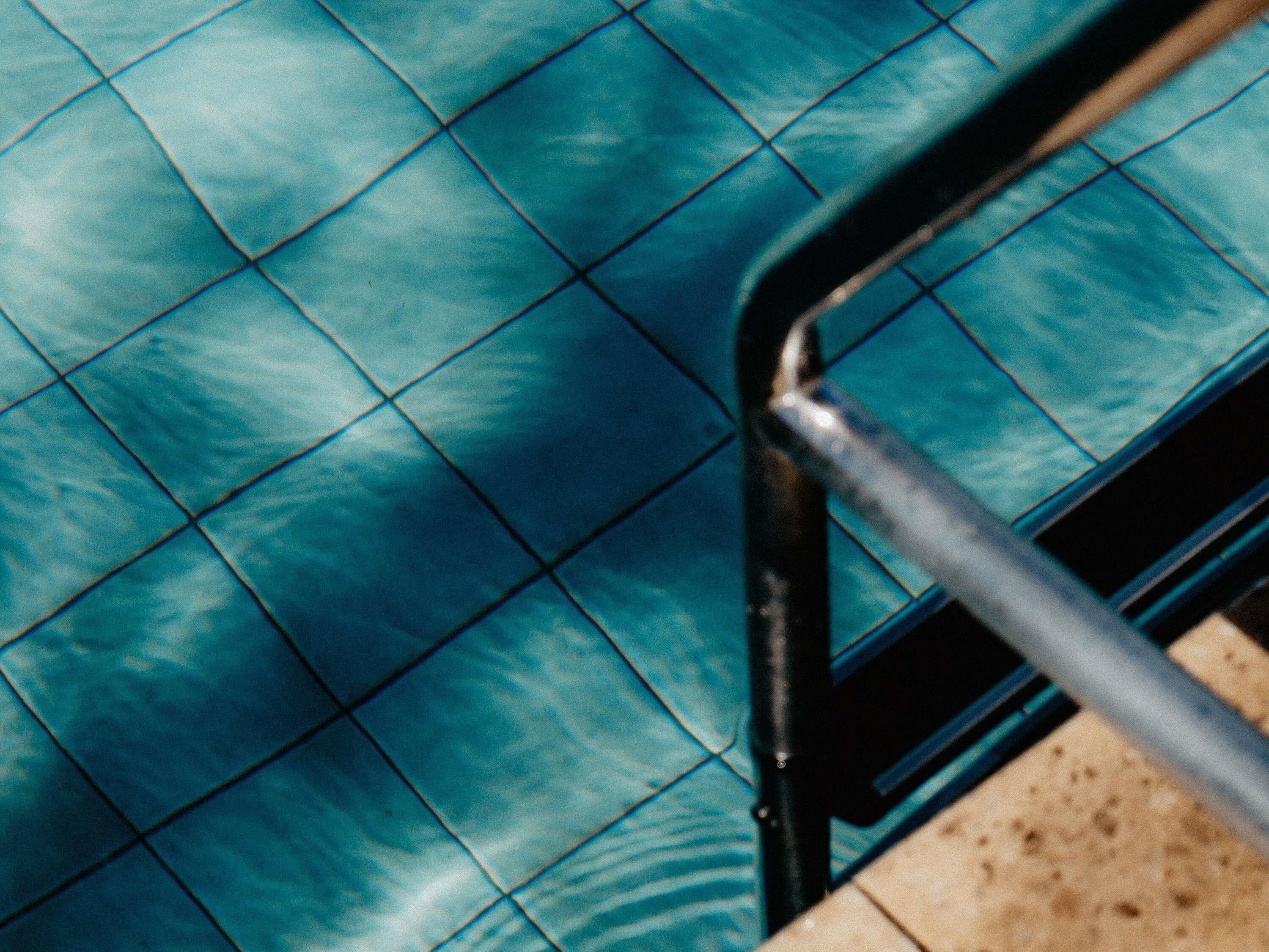 Una piscina con azulejos y una escalera de metal.