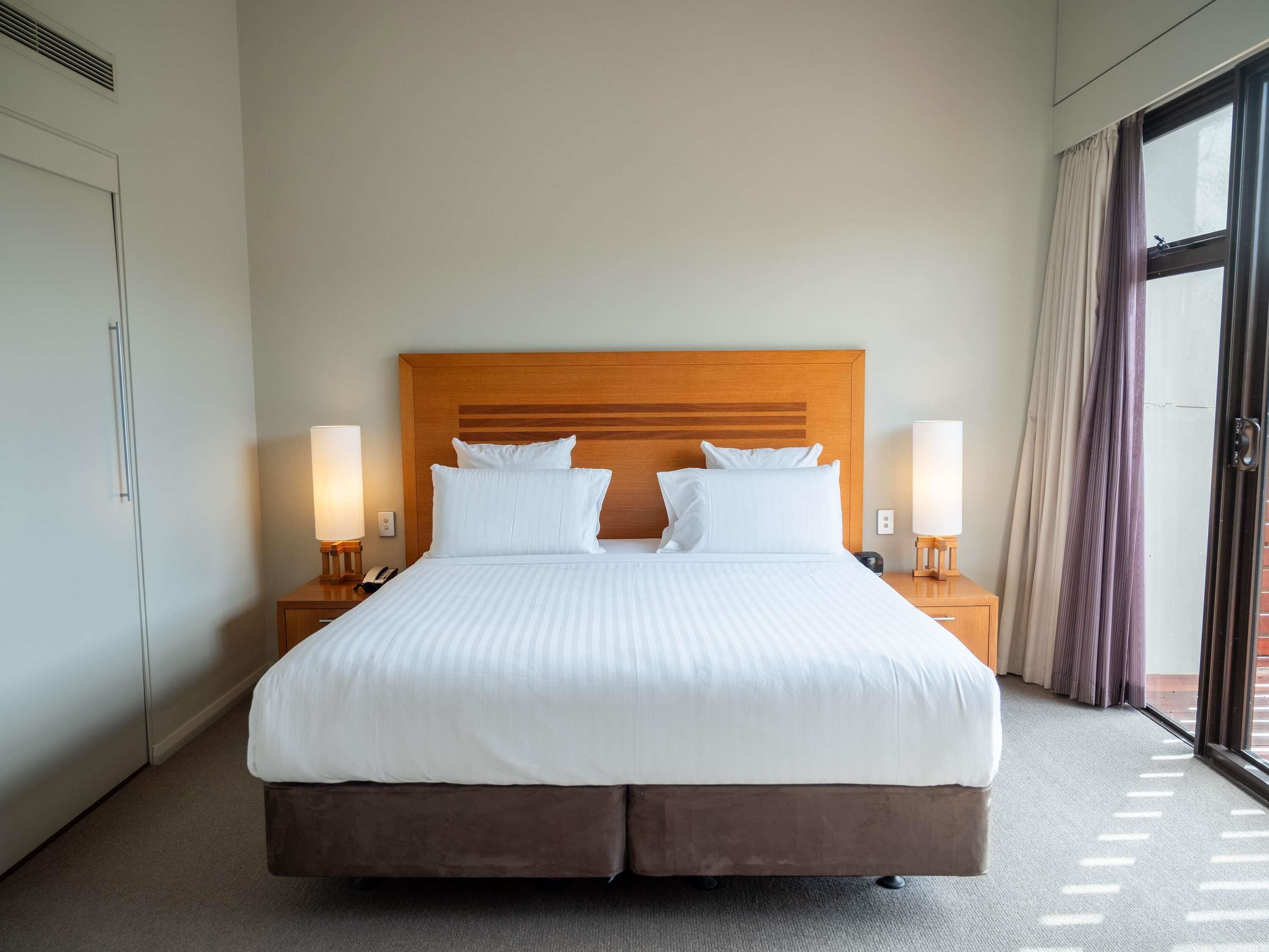 Een hotelkamer met een groot bed, twee nachtkastjes, een houten hoofdbord en uitzicht door een glazen deur.