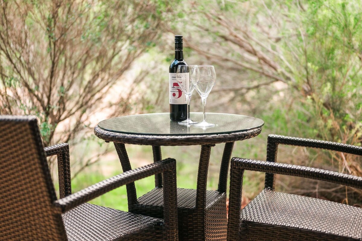 Une table en osier, avec une bouteille de vin et deux verres, entourée de chaises en osier.