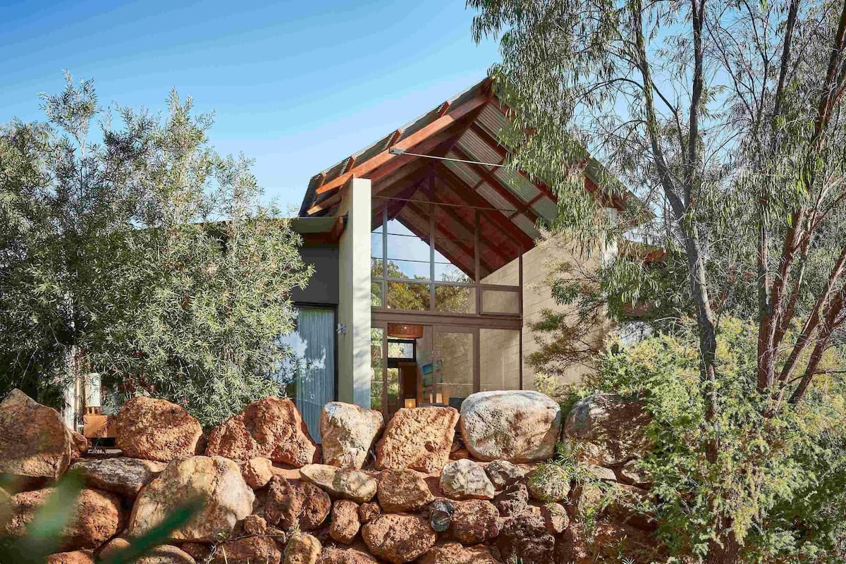 A modern building with a stone wall in front, surrounded by trees.