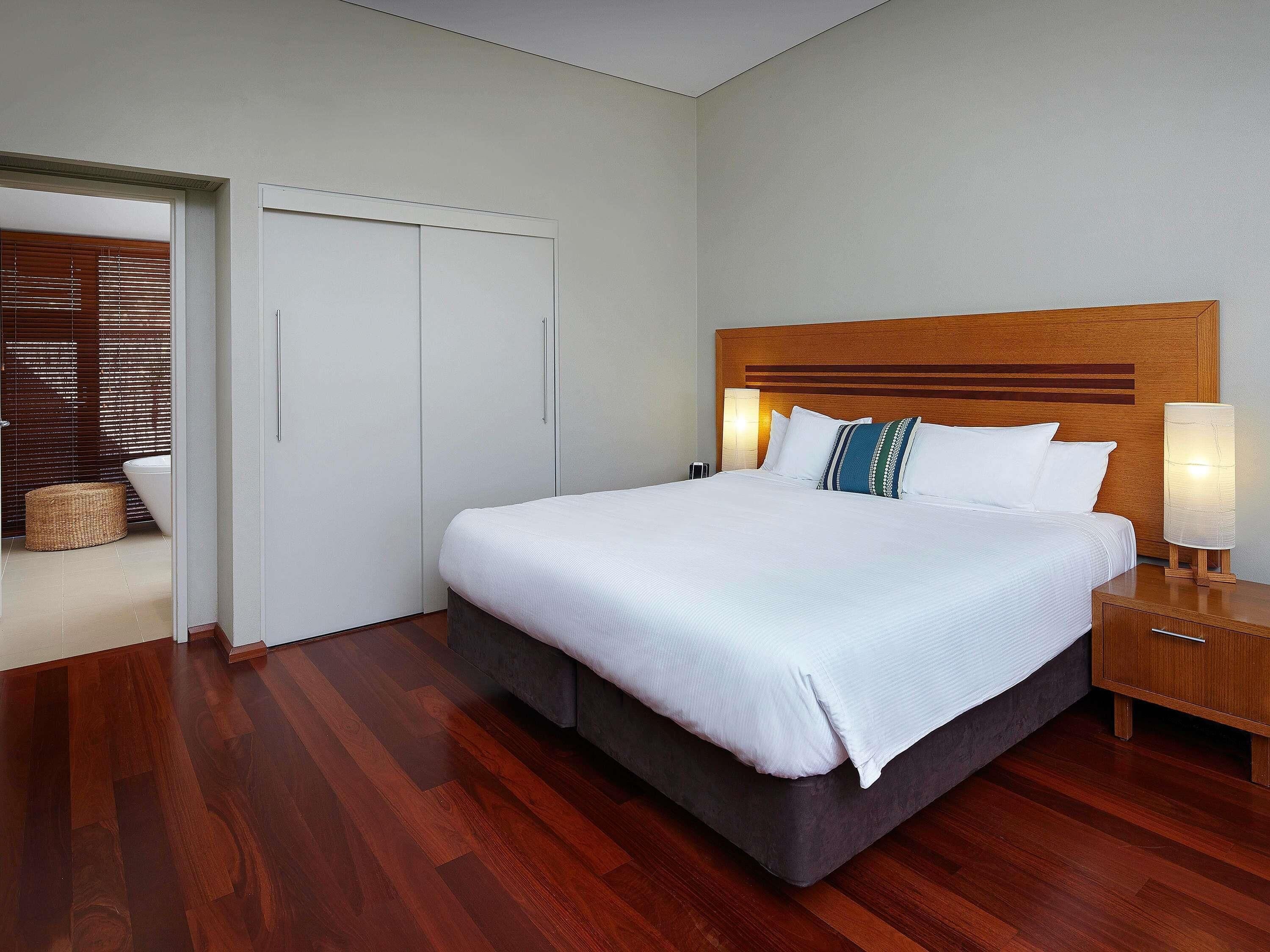 Una habitación de hotel con una cama grande, cabecero de madera, lámparas de noche y un armario.
