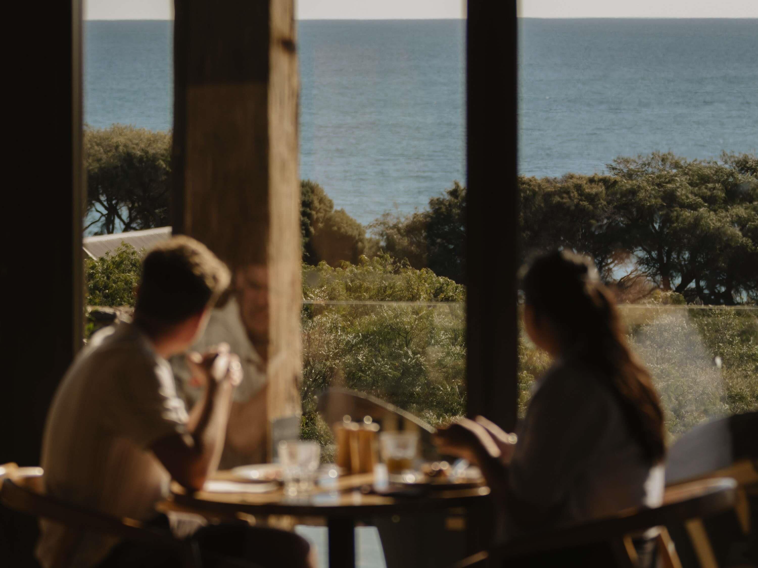 A dining area with a view of the sea, featuring a table with chairs and a glass partition.